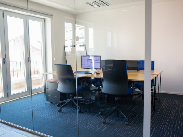 Empty boardroom behind glass wall. Meeting room with conference table, shared desk for team and workplaces. Trading graphs on monitor. Office interior or commercial real estate concept